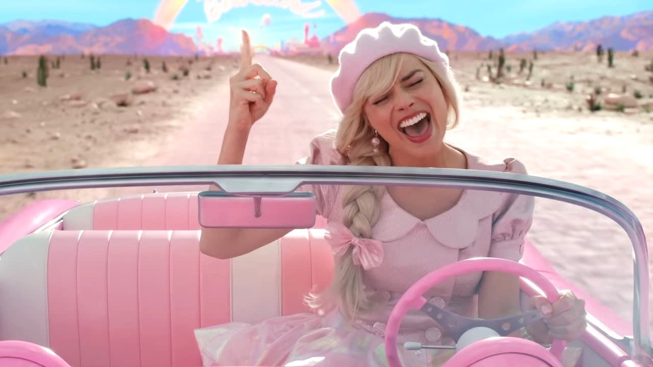 Margot Robbie as Barbie in a pink car, wearing pink, singing, in the Barbie movie.